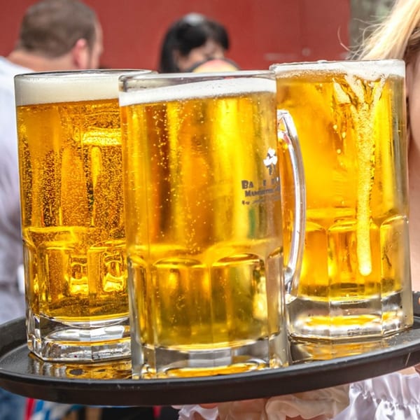 Three large mugs of golden beer with foamy tops on a black serving tray.