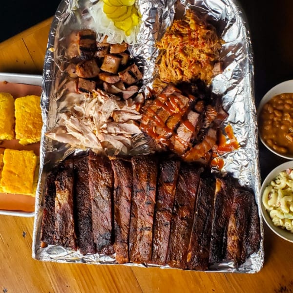 A large platter of KC's Rib Shack BBQ, including ribs, pulled pork, brisket, and sides.
